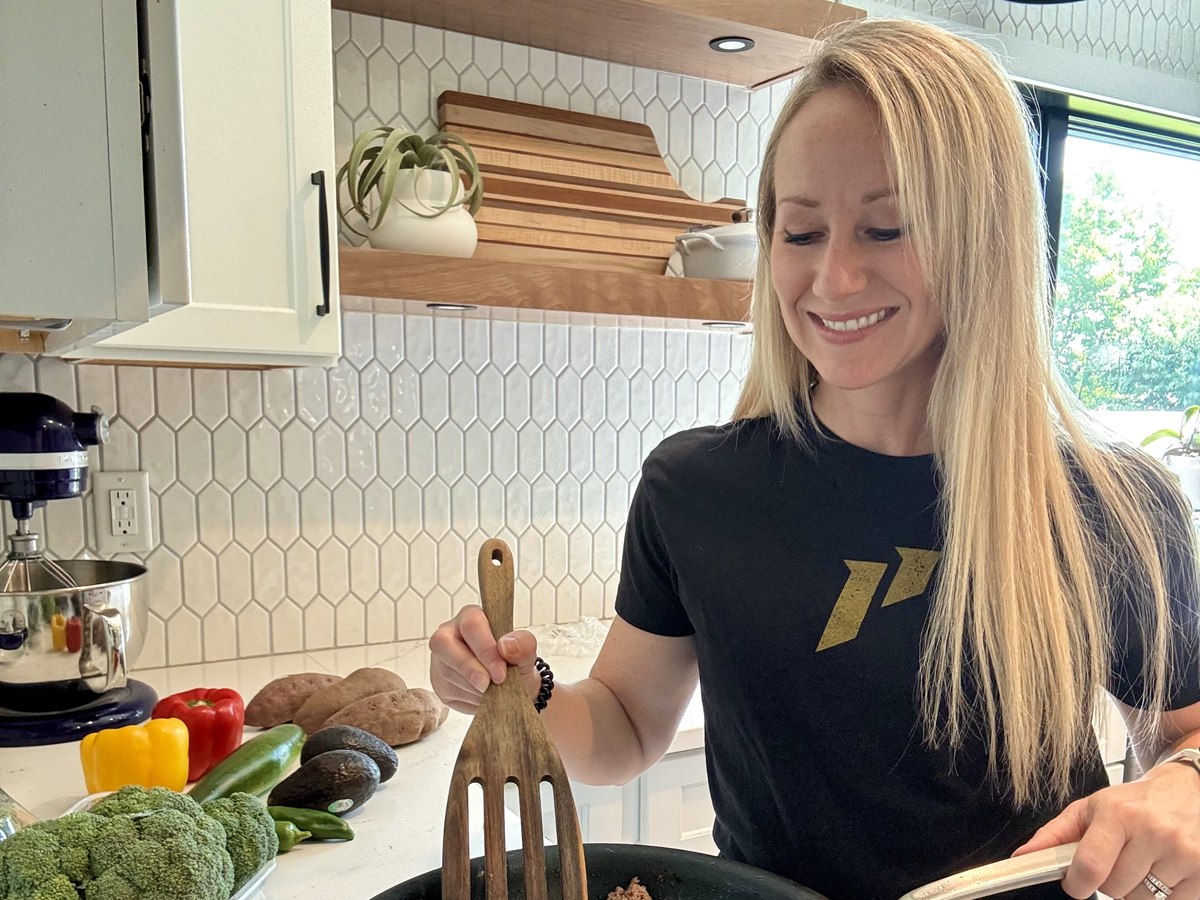 Monica Gleb cooking ground turkey in her kitchen, with peppers, broccoli and potatoes on the counter beside her
